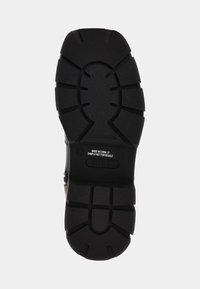 Suola di sneaker nera con motivi di battistrada profondi, gomma testurizzata e dettagli del marchio. Tacco piatto con più scanalature per la trazione.