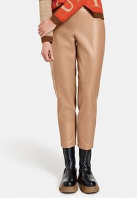 Beiga liknande läderbyxor med slim fit och knäskydd, kombinerat med svarta tunga stövlar med tjock sula.