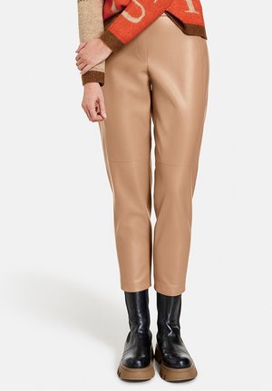 Pantalon en simili cuir beige avec une coupe slim et des coutures aux genoux, associé à des bottes noires chunky avec une semelle épaisse.