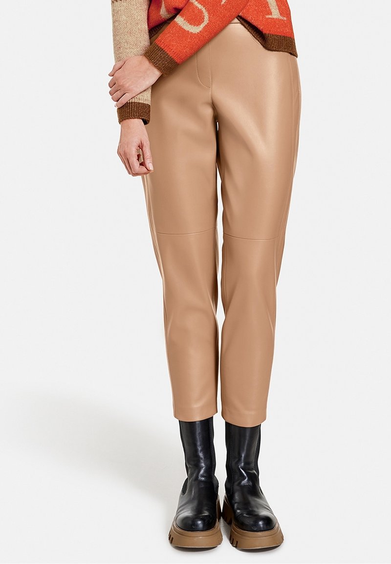 Beiga liknande läderbyxor med slim fit och knäskydd, kombinerat med svarta tunga stövlar med tjock sula.