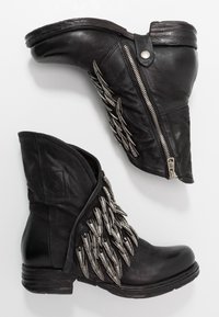 Svarta läderankelstövlar har en asymmetrisk design, texturerade sidodelar som liknar piggar och en detalj med silverdragkedja.