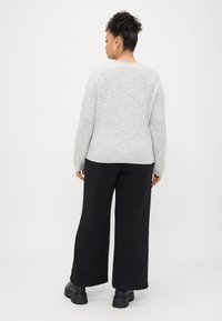 Suéter cinza de malha com um corte descontraído, combinado com calças largas pretas e botas pretas robustas. Tecido texturizado e design simples.