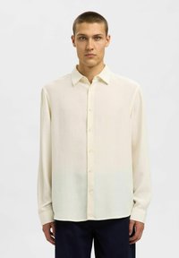 Camicia a maniche lunghe di un tenue crema in tessuto morbido, con chiusura a bottoni, colletto classico e orlo dritto.
