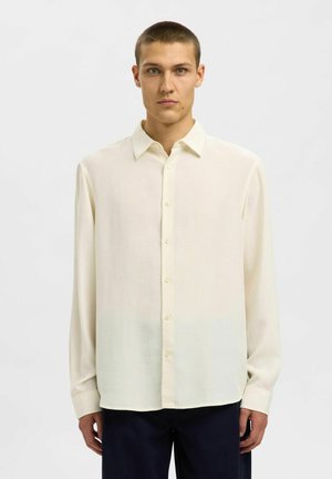Camicia a maniche lunghe di un tenue crema in tessuto morbido, con chiusura a bottoni, colletto classico e orlo dritto.