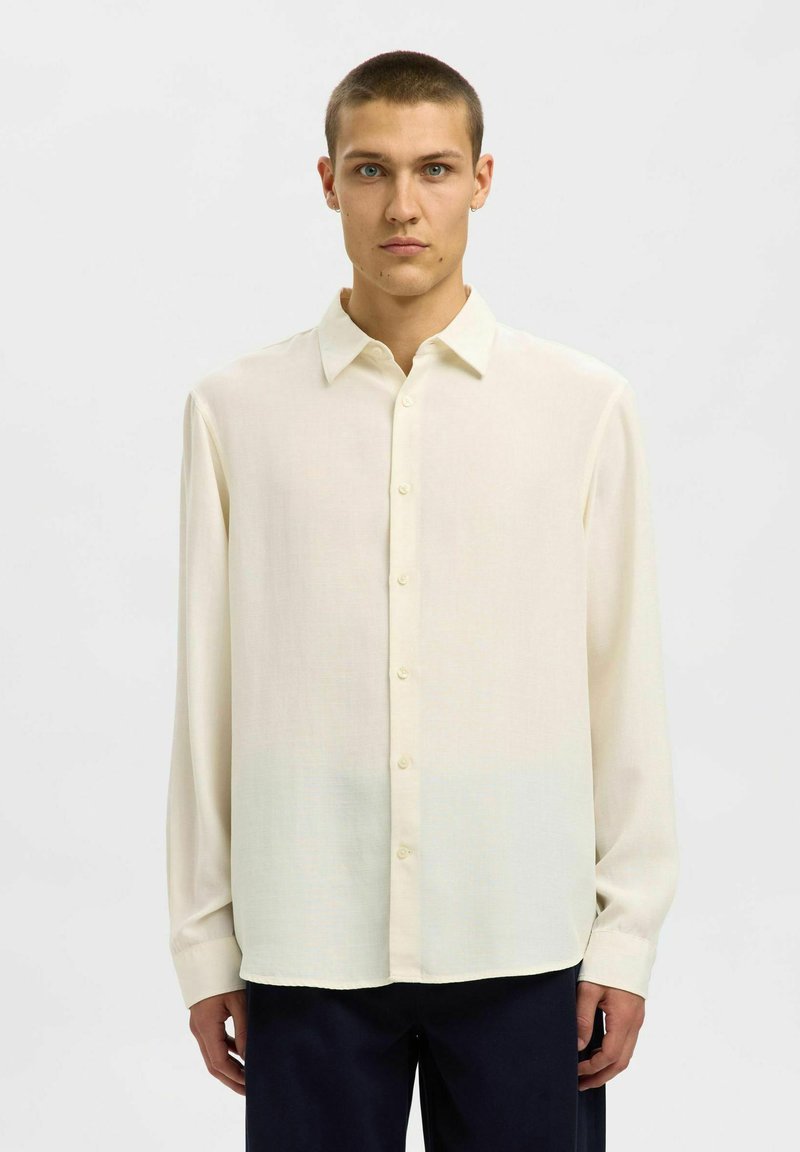 Camicia a maniche lunghe di un tenue crema in tessuto morbido, con chiusura a bottoni, colletto classico e orlo dritto.