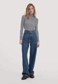 Gestreiftes Langarm-Turtleneck-Oberteil in Schwarz und Weiß, kombiniert mit hoch taillierten, weiten blauen Jeans mit Bindegürtel und Seitentaschen.