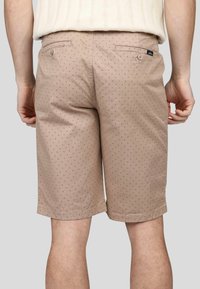 Shorts beige avec un motif subtil de points sombres. Fabriqués en coton, ils disposent de poches arrière et d'une coupe droite. Texture lisse.