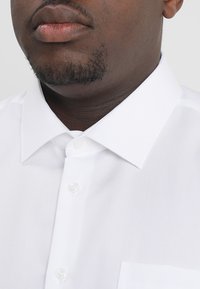 Witte button-up blouse met een puntig kraag, een borstzak en een gladde textuur. Voorzien van doorzichtige kunststof knopen op de knoopsluiting.