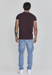 Bordeauxrood t-shirt met witte rand, gecombineerd met lichtblauwe cargobroek met zijzakken en een slim fit. Witte sneakers maken de look compleet.