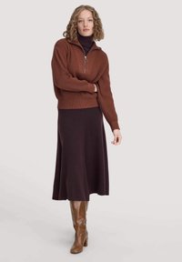 Bruine geribbelde pullover met rits en lange mouwen, gecombineerd met een donkerpaarse flared rok en bruin leren laarzen tot de knie.