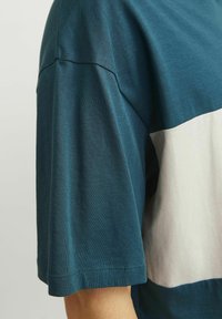 Kortærmet t-shirt i teal med en hvid vandret stribe. Lavet af blødt bomuld, med en afslappet pasform og flade sømme.