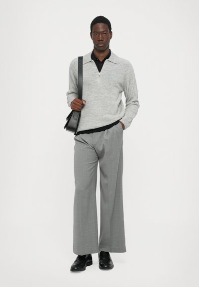 Suéter de punto gris claro con cuello con cremallera, combinado con pantalones de pierna ancha grises. Acentuado por un bolso cruzado negro y zapatos negros.
