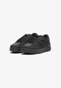 Sapatos desportivos pretos com um upper de couro liso, colarinho acolchoado e design com atacadores. A sola de borracha apresenta padrões de aderência texturizados.