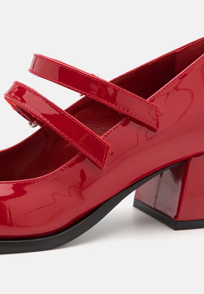 Punane patendiga Mary Jane king, millel on kaks reguleeritavat rihma, plokknõlv ja sile pind, ümar toe disain.