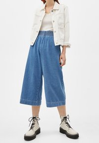 Blå denimculotter med elastisk midja, matchat med en vit kort denimjacka och krämfärgade snörstövlar.