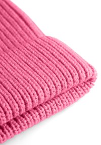 Geribbelde roze gebreide stof met twee overlappende secties, die een textuurpatroon vertoont en gemaakt is van zachte, dikke garen.