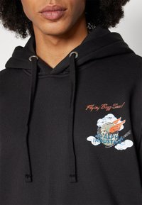 Sweat à capuche noir en coton avec une poche kangourou. Présente un motif graphique avec des nuages et des ailes, ainsi qu'un cordon de serrage avec des éléments métalliques argentés.