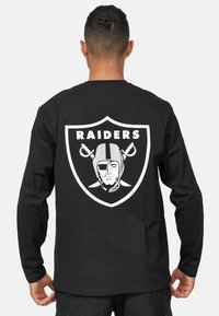 Svart långärmad t-shirt med en stor vit Raiders-logotyp på baksidan, inklusive en styliserad hjälm och korslagda svärd.