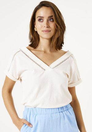 Haut blanc à manches courtes avec un col en V, doté d'un tissu texturé et de coutures décoratives le long de l'encolure. Accompagné d'un pantalon bleu clair.