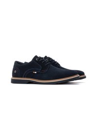 Zapatos de ante azul marino con cordones y suela de goma. Presentan costuras en contraste y un pequeño emblema en el talón. Diseño clásico de punta redonda.