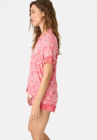 Roze pyjama set met bloemenpatroon, bestaande uit een top met korte mouwen en kantafwerking, en bijpassende shorts met gegolfde accenten. Soepele stoftextuur.