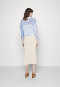 Camisa listrada em azul claro com as costas lisas, combinada com uma saia rodada texturada em creme, até aos joelhos. Sapatos de salto grosso castanhos completam o visual.