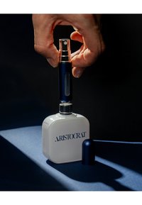 Hvid rektangulær beholder med teksturerede kanter, blå accenter og "ARISTOCRAT"-logo. Blåt spraydæksel er ved at blive monteret. Mørk baggrund.