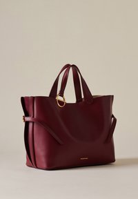 Burgundy leather tote bag with two top handles, a circular gold accent, and side pockets. Smooth texture with a structured design.