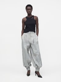 Femme portant un haut noir sans manches et un pantalon ample à carreaux gris, resserré aux chevilles, associé à des chaussures noires à talons hauts.
