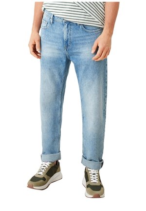 Partie inférieure du corps d'une personne portant un jean bleu clair retroussé, des baskets vert olive et blanc, et une chemise rayée rentrée.