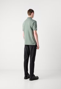 Polo skjorte i salviegrønn, kortermet, med kragehals. Kombinert med svarte jeans og svarte sko, sett fra baksiden.
