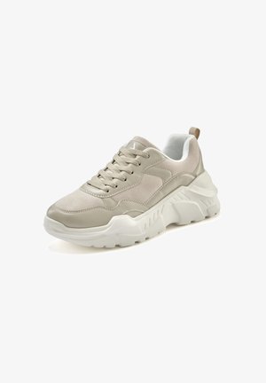 Beige athletic sneakers with a textured upper, smooth panels, white chunky sole, and lace-up closure. Features a rear pull tab.
