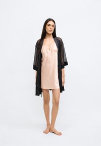 Μαύρο κιμονό από δαντέλα πάνω από ανοιχτό ροζ σατέν φόρεμα-λίπανση με μέση αυτοκρατορικού στυλ και διακοσμητικούς ιμάντες, φορεμένο με γυμνά πόδια. Απαλή υφή και διαφανείς λεπτομέρειες.