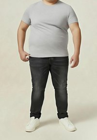 Maglietta grigia a maniche corte abbinata a jeans scuri e sneaker bianche. L'abbigliamento presenta un design aderente e texture lisce.