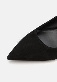 Chaussure noire en daim à bout pointu avec une finition texturée et un décolleté bas, dévoilant une partie du pied, dotée d'une doublure intérieure lisse.