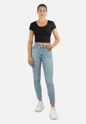 Schwarzes, kurzes T-Shirt mit kurzen Ärmeln, kombiniert mit hellblauen, hoch taillierten Jeans und weißen Sneakern, die einen lässigen Look zeigen.