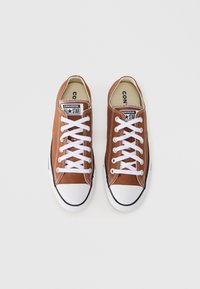 Καφέ πάνινα αθλητικά παπούτσια με λευκά κορδόνια, λαστιχένιο κάλυμμα στα δάχτυλα και μαύρες λεπτομέρειες. Διαθέτουν την επωνυμία Converse All Star στη γλώσσα. Επίπεδη σόλα.