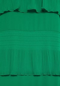 Tessuto verde con una trama rigata e dettagli arricciati. Presenta sezioni lisce e plissettate e un design solido, creando un effetto stratificato.