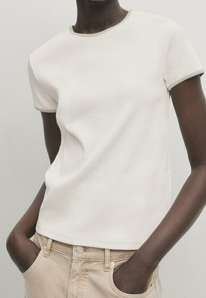 Maglietta bianca a maniche corte con scollo rotondo e bordi beige a contrasto, abbinata a jeans beige chiaro.