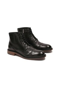 Botas de tobillo de cuero negro con cierre de cordones y cremallera lateral, punta redondeada, suela marrón en contraste, textura suave y detalles con puntera.
