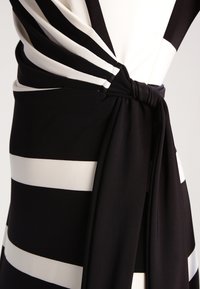 Abito a righe bianche e nere, caratterizzato da un design avvolgente con vita annodata. Tessuto morbido con righe spesse alternate, texture liscia.