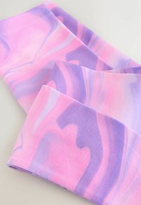 Tkanina legginsów wielokolorowa, różowo-fioletowa, o gładkiej, miękkiej fakturze i wirującym marmurkowym wzorze. Mieszanka bawełny, w złożonym układzie.