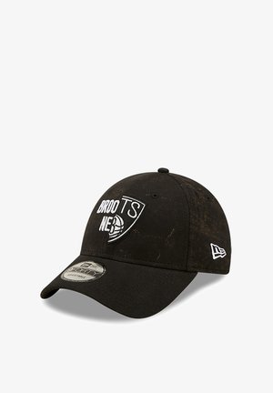 Black cap with a curved brim, featuring a white logo design and textured fabric. Adjustable strap at the back for fit.