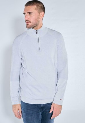 Hellgrauer Pullover mit Reißverschluss am Kragen, Rippstruktur und kontrastierenden Einsätzen. Verfügt über lange Ärmel und eine figurbetonte Silhouette.