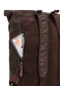 Bruine leren en stoffen rugzak met een zijrits zak waar een smartphone gedeeltelijk zichtbaar is. Stevige schouderbanden met een gestructureerd detail.