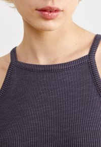 Mörklila ribbat linne med tunna axelband och rak halsringning, med en texturerad tygkvalitet och synliga sömsdetaljer.