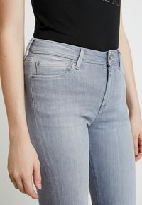 Světle šedé džínové kalhoty s pětiprůstkovým designem, s jemným vyblednutím a hladkou texturou. Pas je vybaven poutky na opasek a stříbrnými kovy.