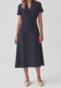 Marineblauwe midi-jurk met korte mouwen, ceintuur in de taille en een omgeslagen kraag; gladde textuur en vloeiend ontwerp.