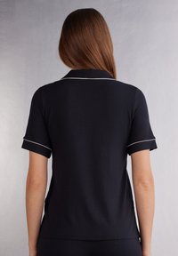 Marineblauwe polo met korte mouwen, voorzien van een klassieke kraag en witte bies langs de mouwen en kraag, gemaakt van een gladde, lichte stof.