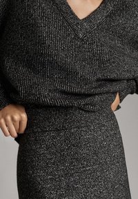 Schwarz-weißer Strickpullover mit V-Ausschnitt und geripptem Saum, kombiniert mit einem passenden figurbetonten Rock, der einen strukturierten Stoff zeigt.